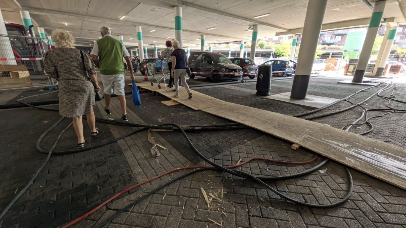 People walking on a makeshift wooden walkway surrounded by loose cables in a supermarket construction zone, highlighting safety hazards and trip risks